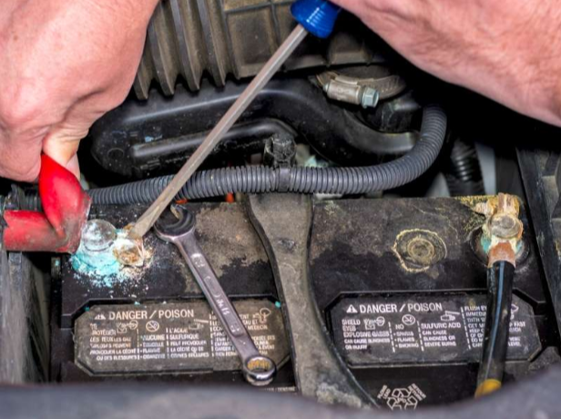Picture of a corroded battery. A person is disconnecting the positive terminal.