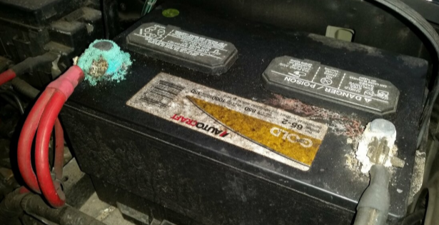 Picture of a vehicle battery. The battery is corroded on the positive terminal.