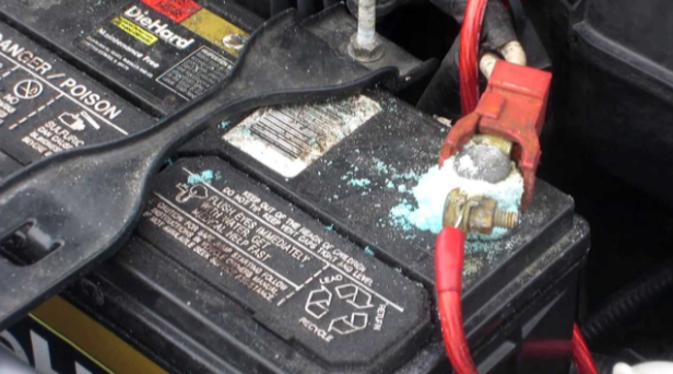 Picture of a vehicles battery. The battery is corroded on the positive terminal.