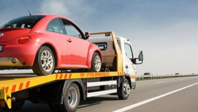 Picture of a red beetle being towed on a flatbed tow truck.