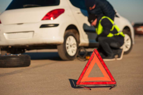 Picture of a Towing Coquitlam tow truck operator repairing a flat tire on a white vehicle on the side of the road. The are is delineated with a red cone.