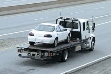 Picture of a white flatbed tow truck carrying a white car on its bed.