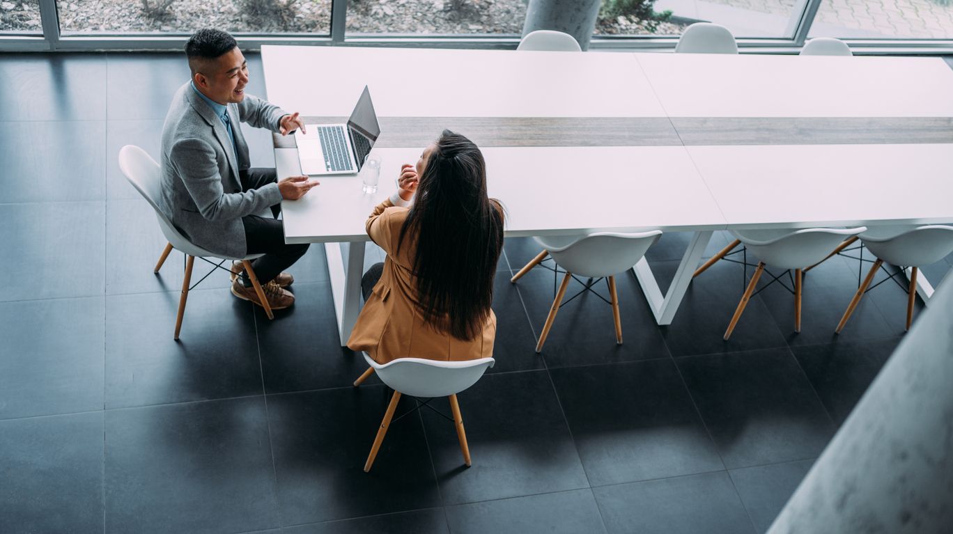 A man and a woman are sitting at a table with a laptop.