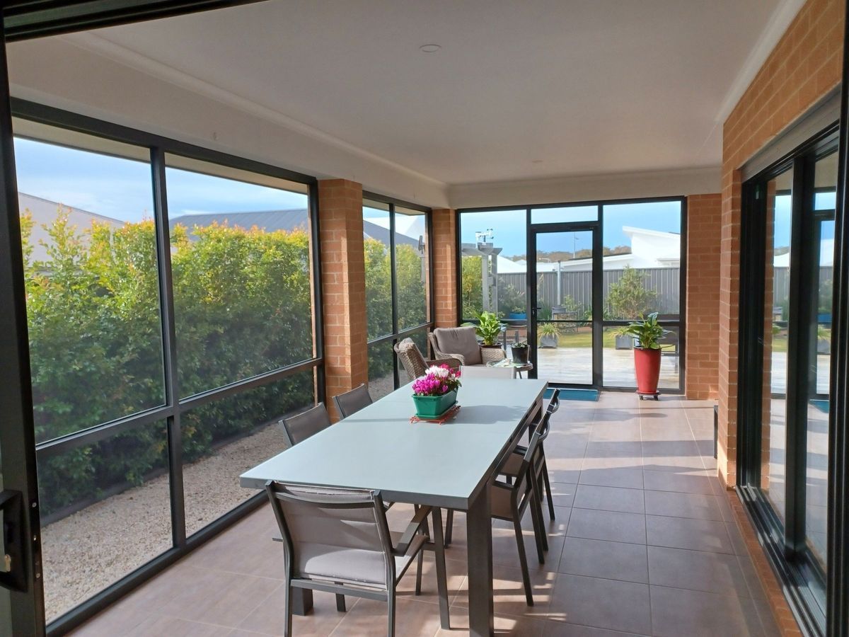 Sunroom with long table and chairs, surrounded by windows overlooking a garden.