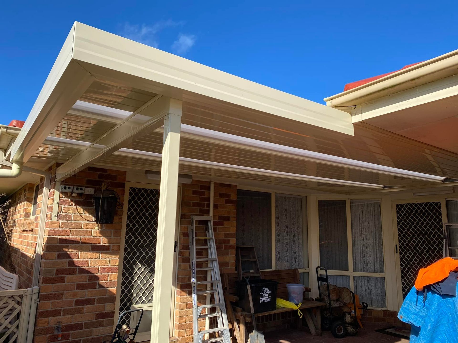 Sun shining through a slatted white pergola roof against a blue sky.
