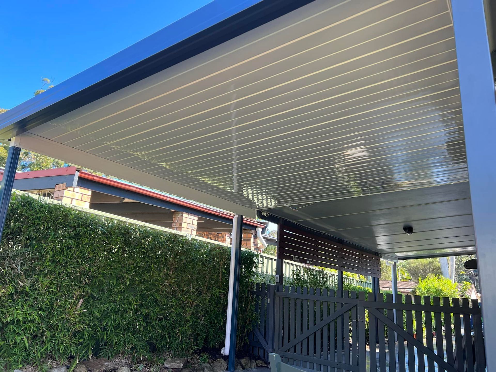 A white patio cover is being installed on the side of a brick house.