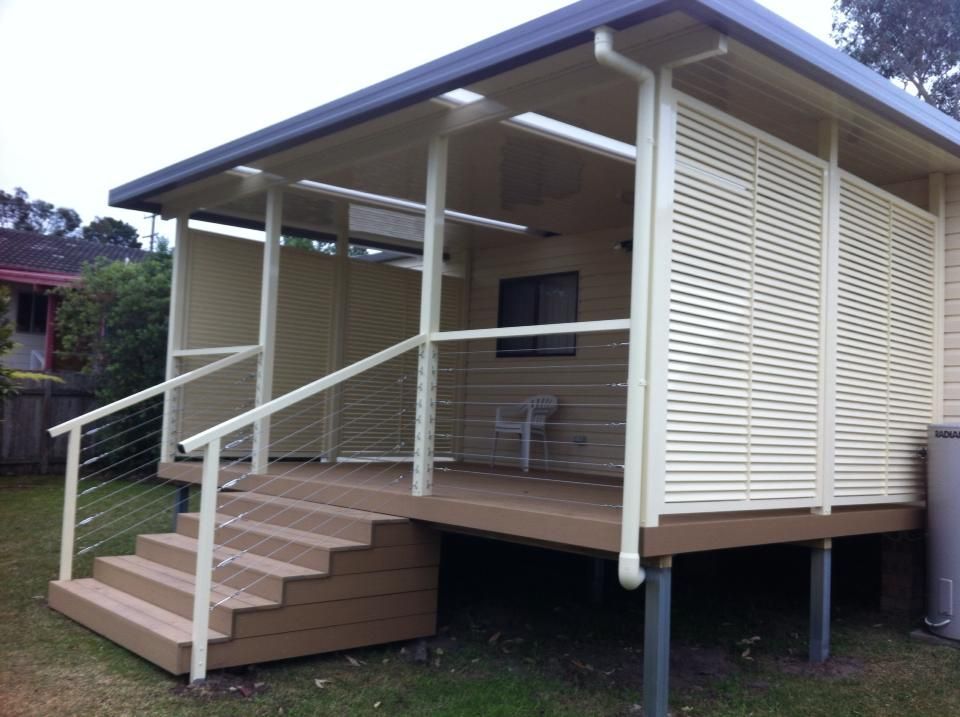 Beige louvered panels on a porch next to a house with water heater and fence in a yard.