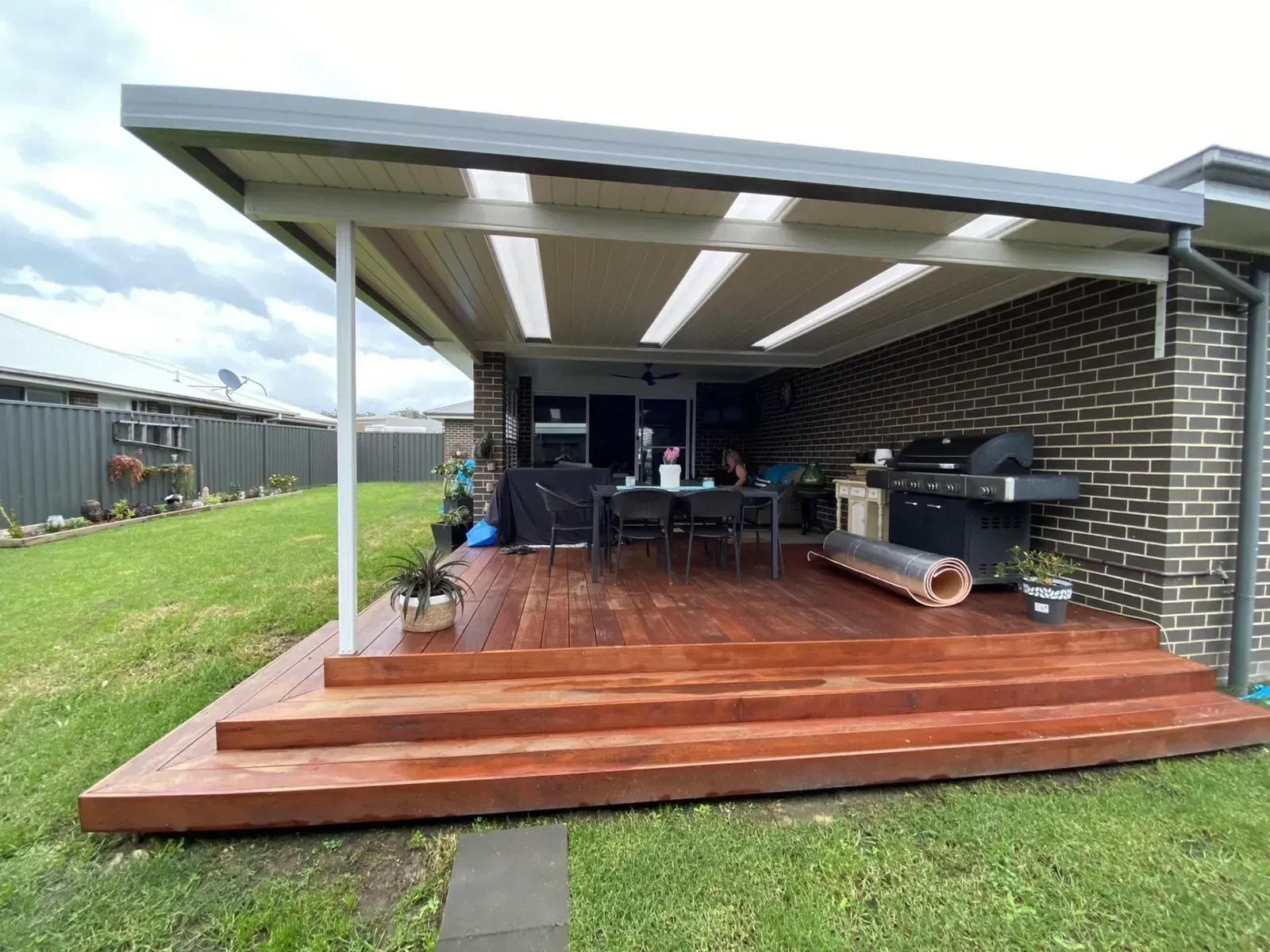 Wooden deck with a covered patio, a brick wall, and a lawn in the backyard.