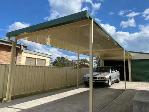 Car under a carport, beige and green, next to a fence and garage.