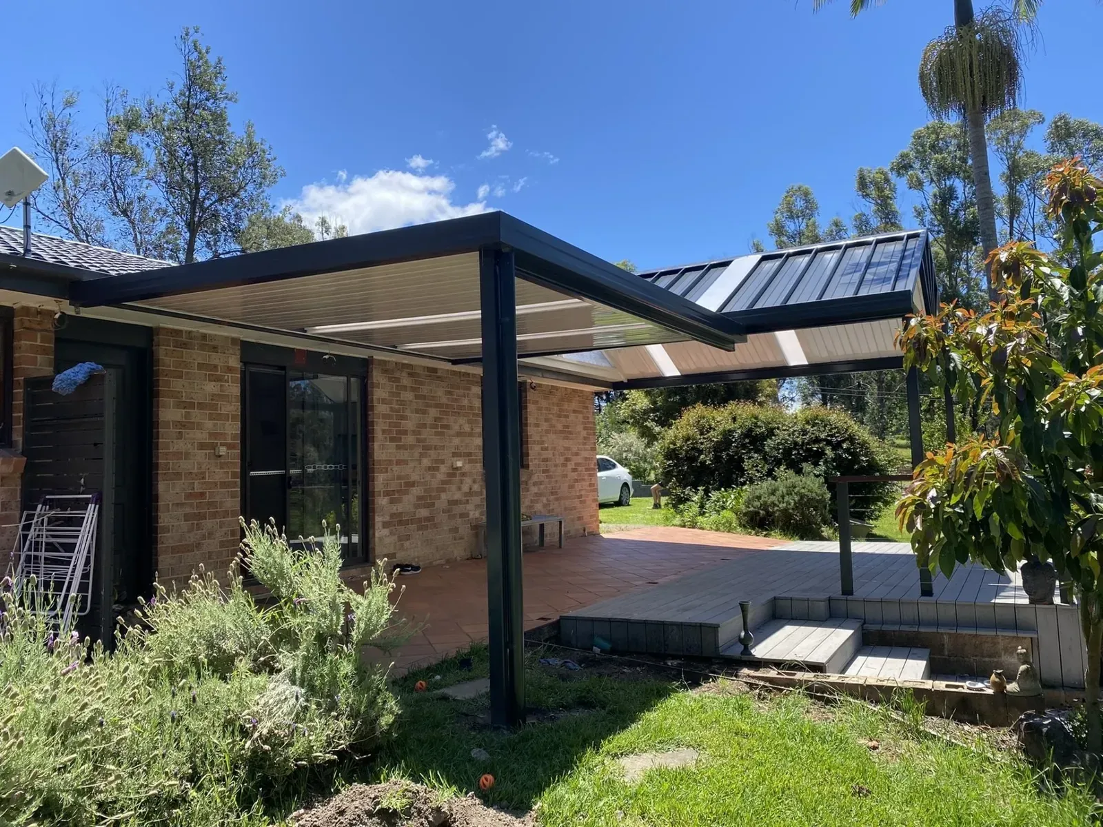 Patio with black frame, light panels, brick house, and greenery.