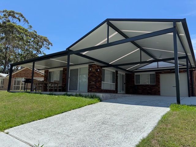 Wooden pergola over a patio with grass and trees in the background on a sunny day.