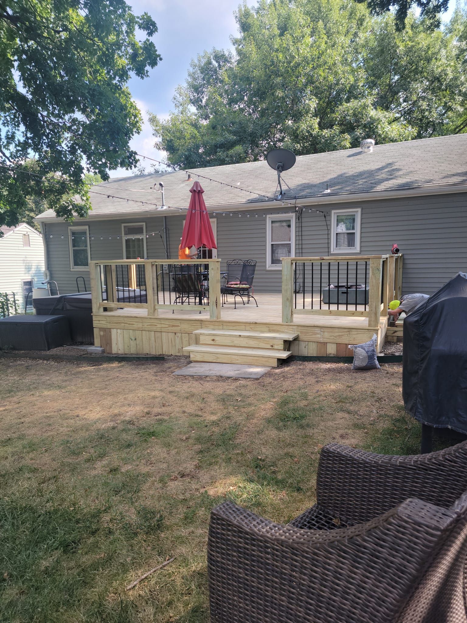 Backyard deck with black railings, a red umbrella, and seating; the yard has dry grass.