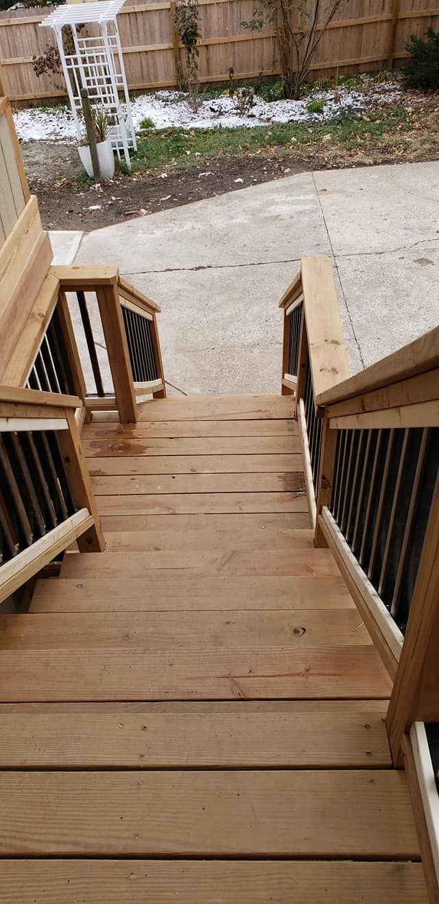 Wooden staircase leading down to a concrete patio and backyard, with black railing.