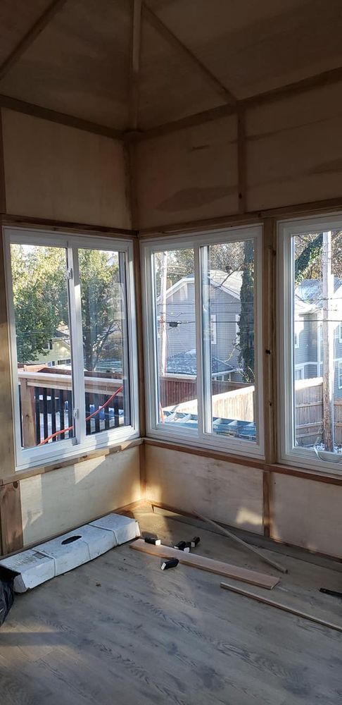 Interior view of a sunroom under construction, with wooden framing, windows, and flooring.
