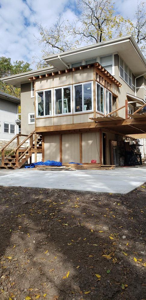 House under construction with new concrete pad, surrounded by dirt and trees.