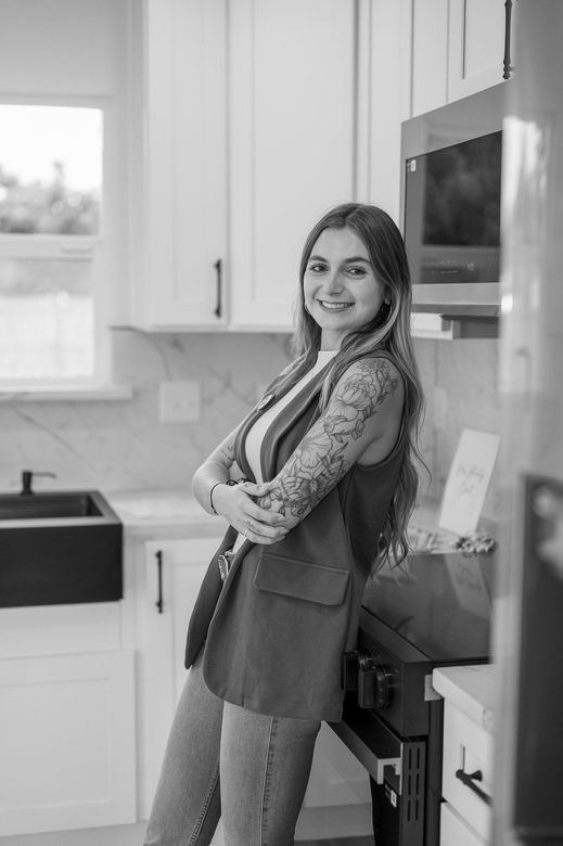 Woman in blazer, smiling, arms crossed, leaning against a built-in oven in a white kitchen.