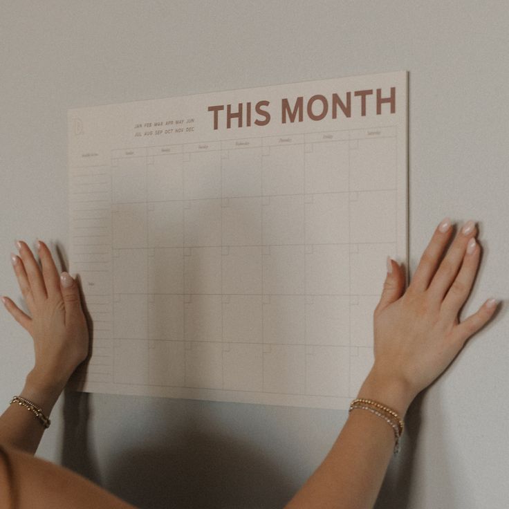 Hands hanging a monthly calendar on a wall. The calendar is tan with the words
