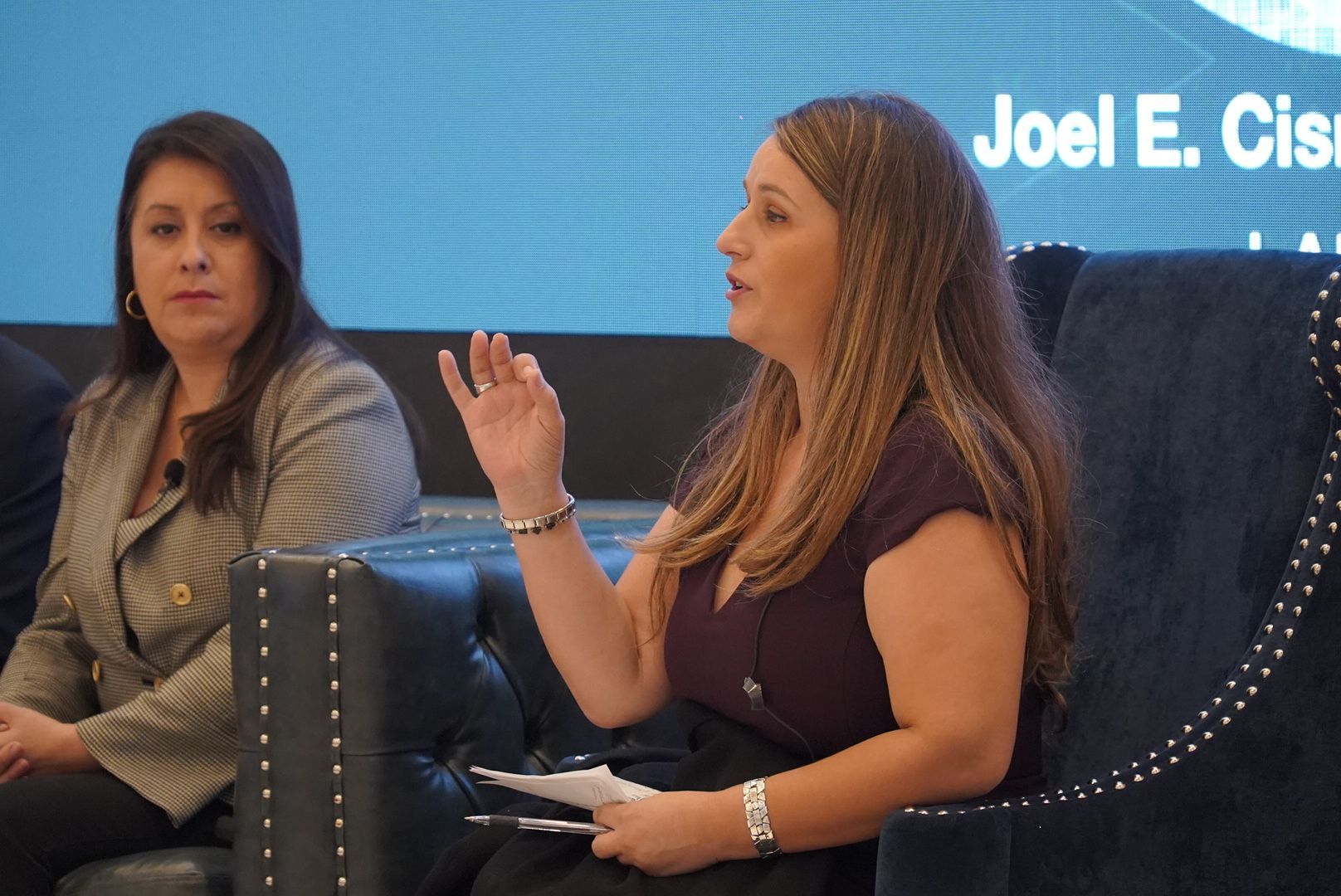 Two women are sitting in chairs in front of a screen that says joel e. clark