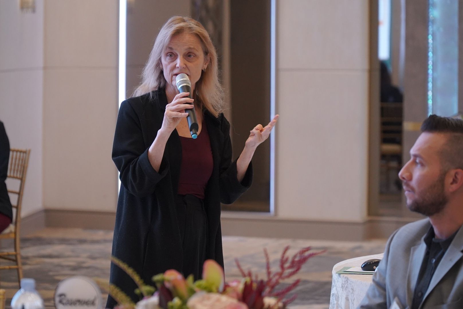 A woman is holding a microphone in front of a man sitting at a table.