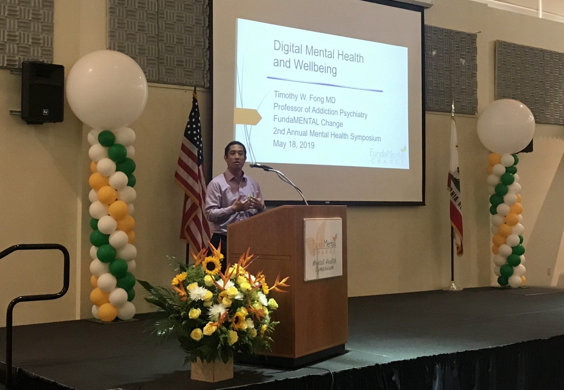 A man is standing at a podium giving a presentation in front of a large screen.