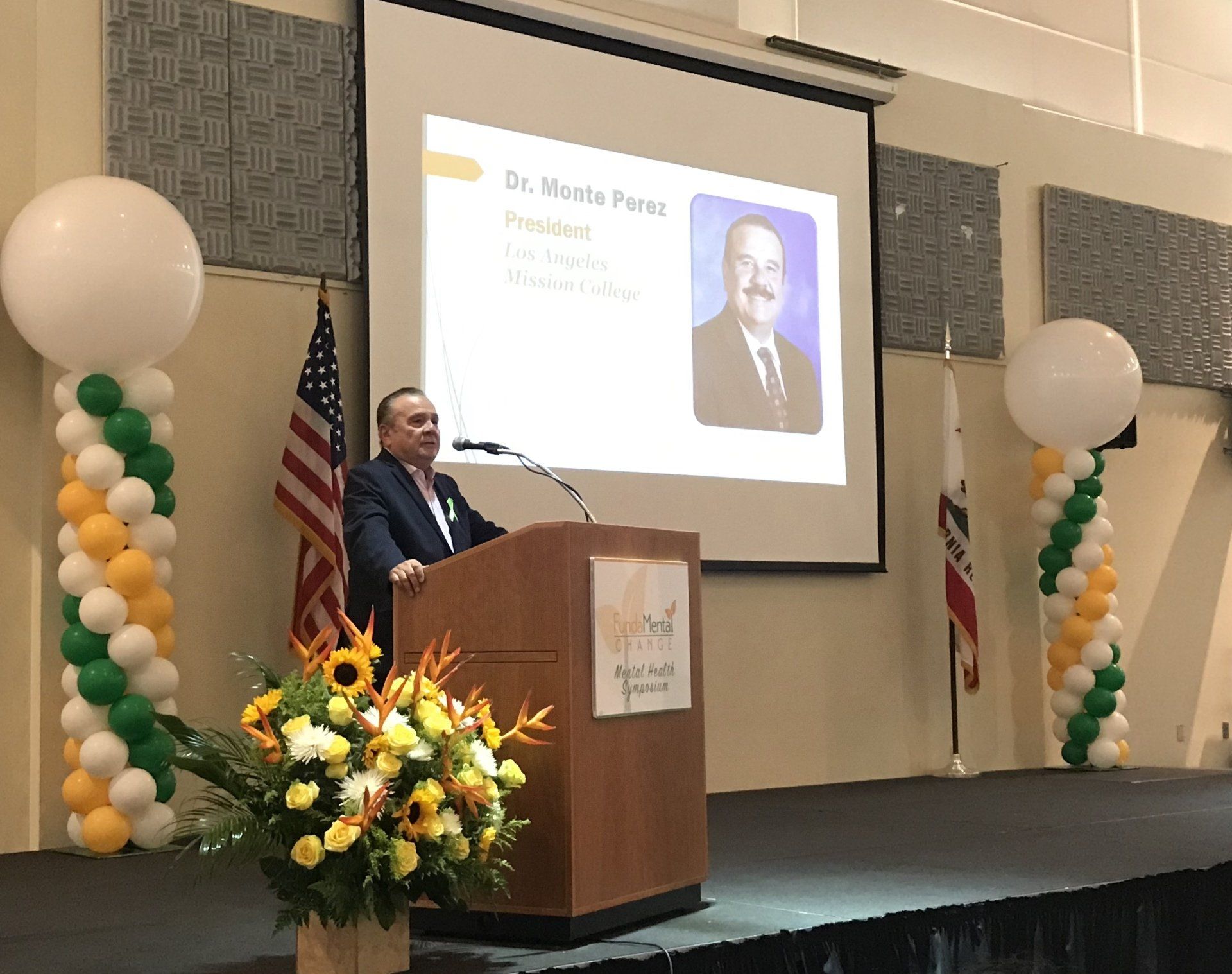 A man is giving a speech at a podium with balloons in the background