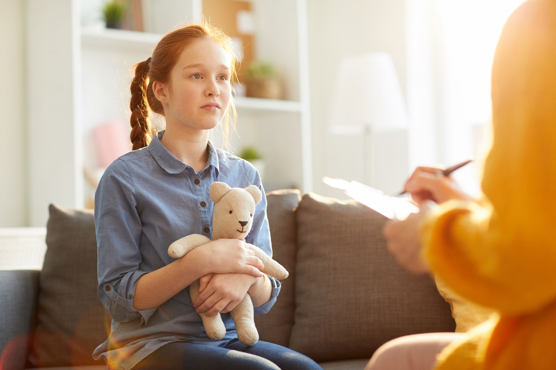 A young girl is sitting on a couch holding a teddy bear.