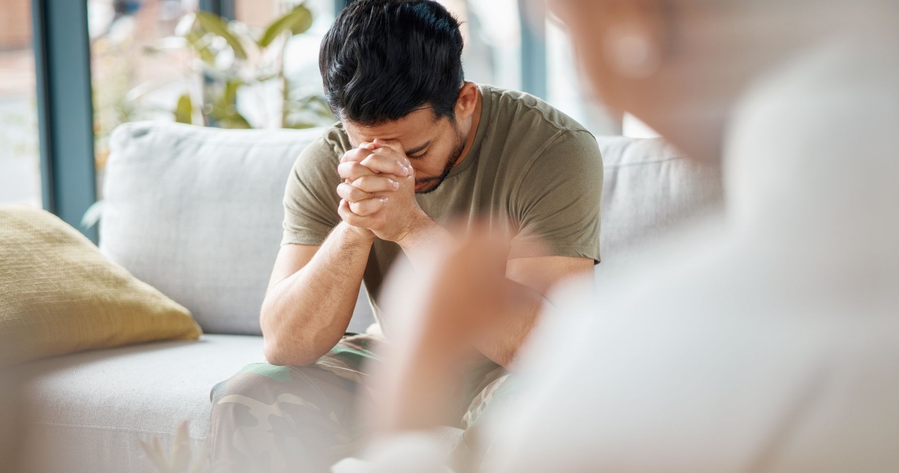 a man is sitting on a couch with his hands folded in prayer