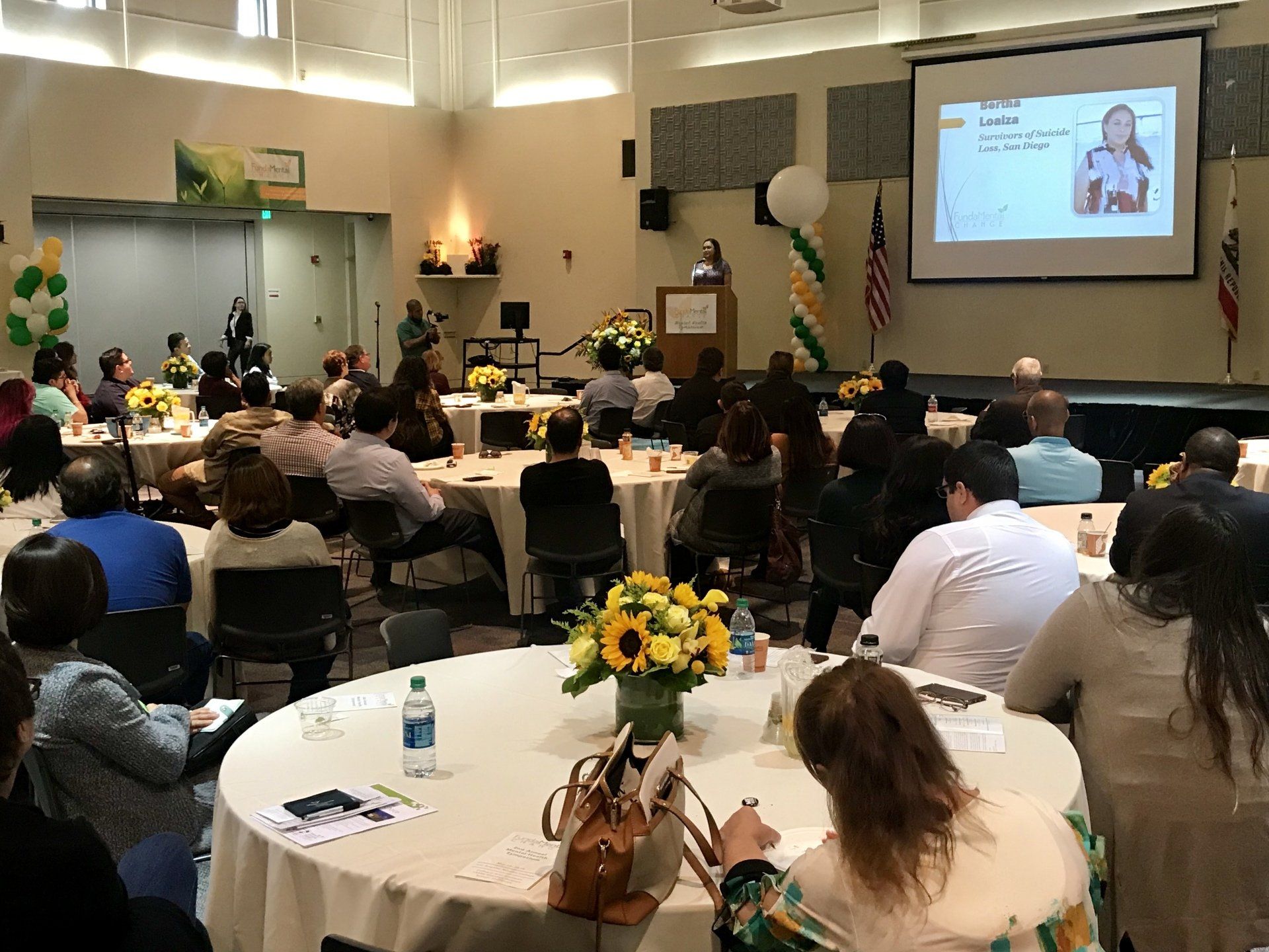 A group of people are sitting at tables in a room watching a presentation.