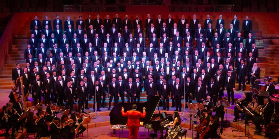 A large choir and orchestra are performing on a stage