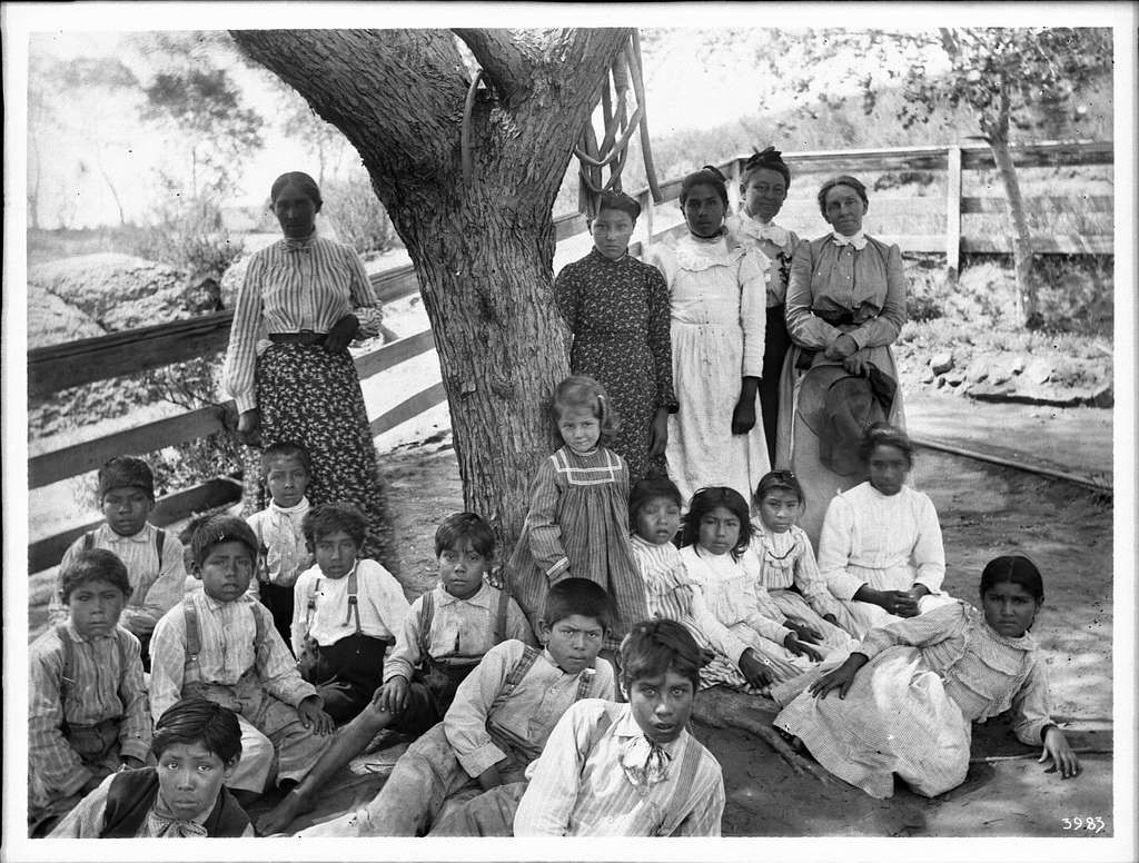 a black and white photo of a group of children sitting under a tree