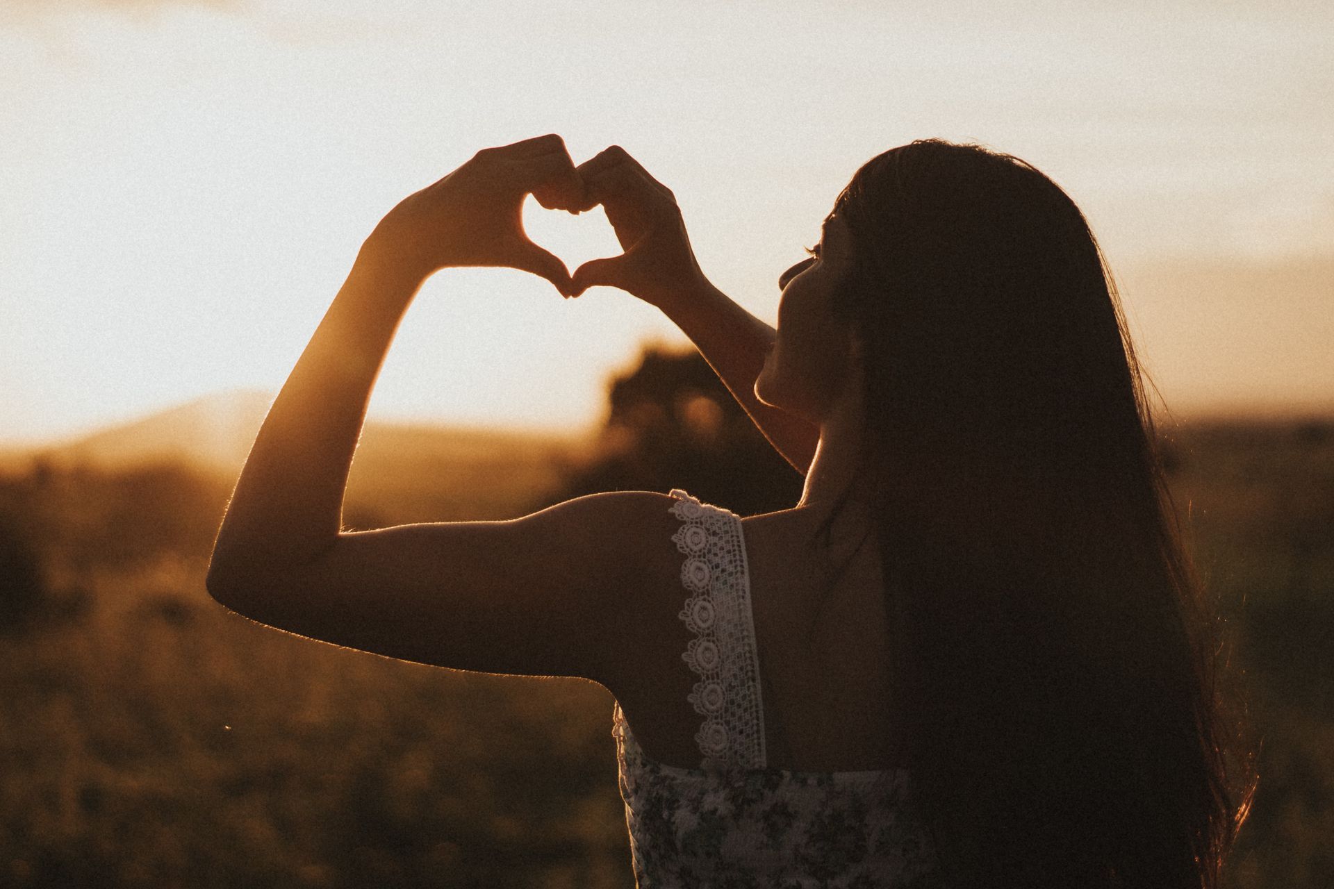 a woman is making a heart shape with her hands at sunset