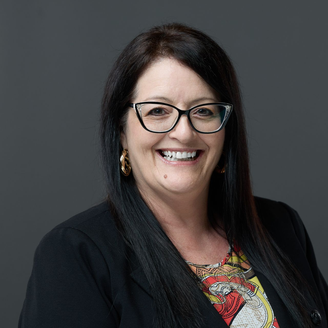 A woman in a suit and white shirt is smiling for the camera.