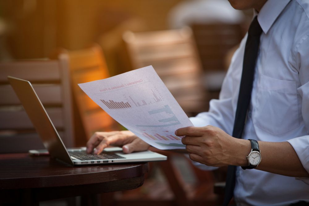 A Man is Sitting at a Table Using a Laptop and Holding a Piece of Paper — Rauseo Group in Zuccoli, NT