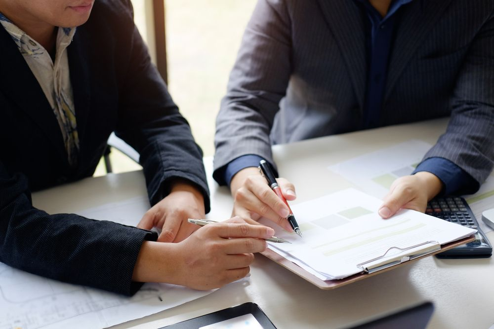 Two people sitting at a desk looking at notes of a clipboard