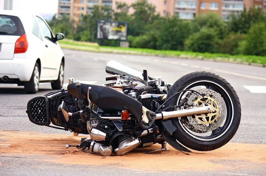 A motorcycle has crashed into a car on the side of the road.