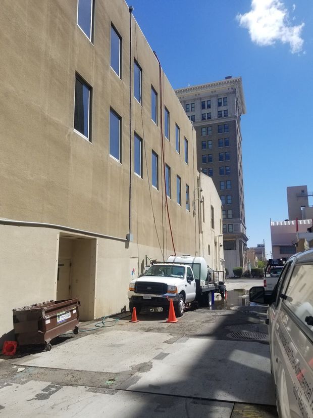 Narrow urban alley beside a beige building, with parked vans, orange cones, and a tall tower in the distance