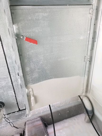 Metal hatch or window with frosted glass and a red handle in a gray industrial setting