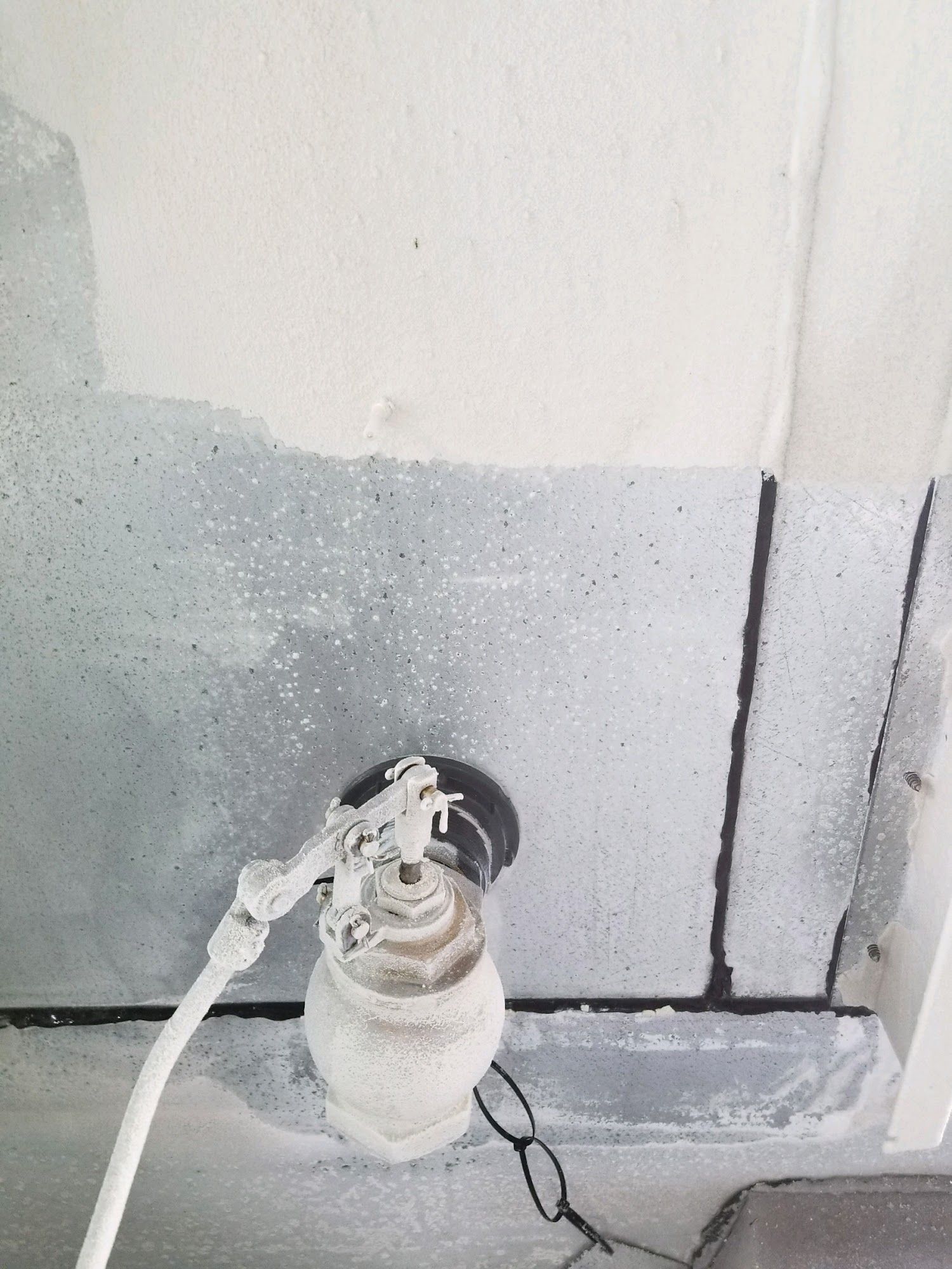 A gas cylinder with attached hose and regulator against a white wall with gray lower paint.