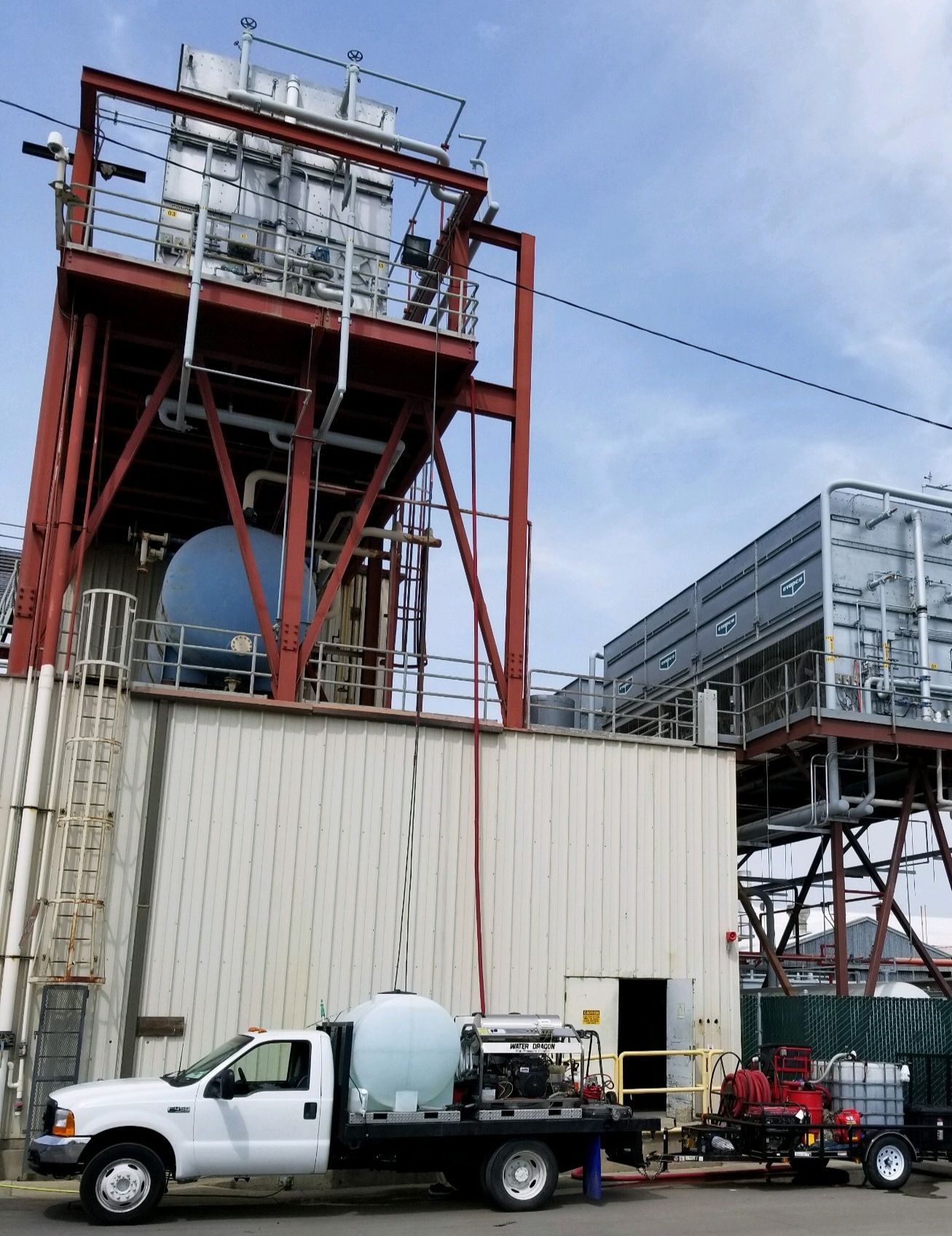 Industrial site with a white utility truck, red rigging, and large machinery under a cloudy sky