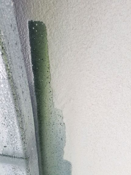 Close-up of a green vertical strip on a textured white wall with a gray edge on the left.