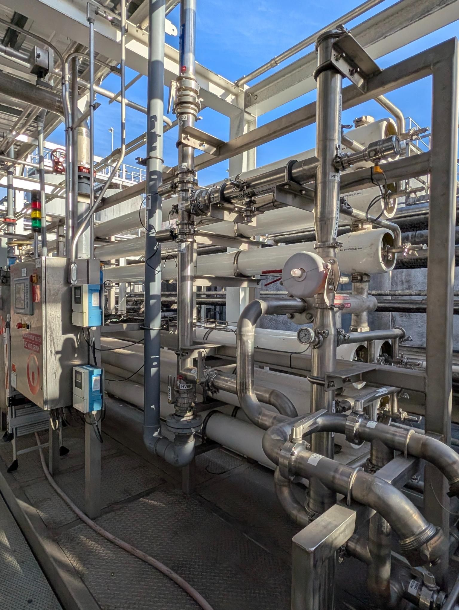Industrial pipes and valves in a metal plant, with a worker standing on the left side