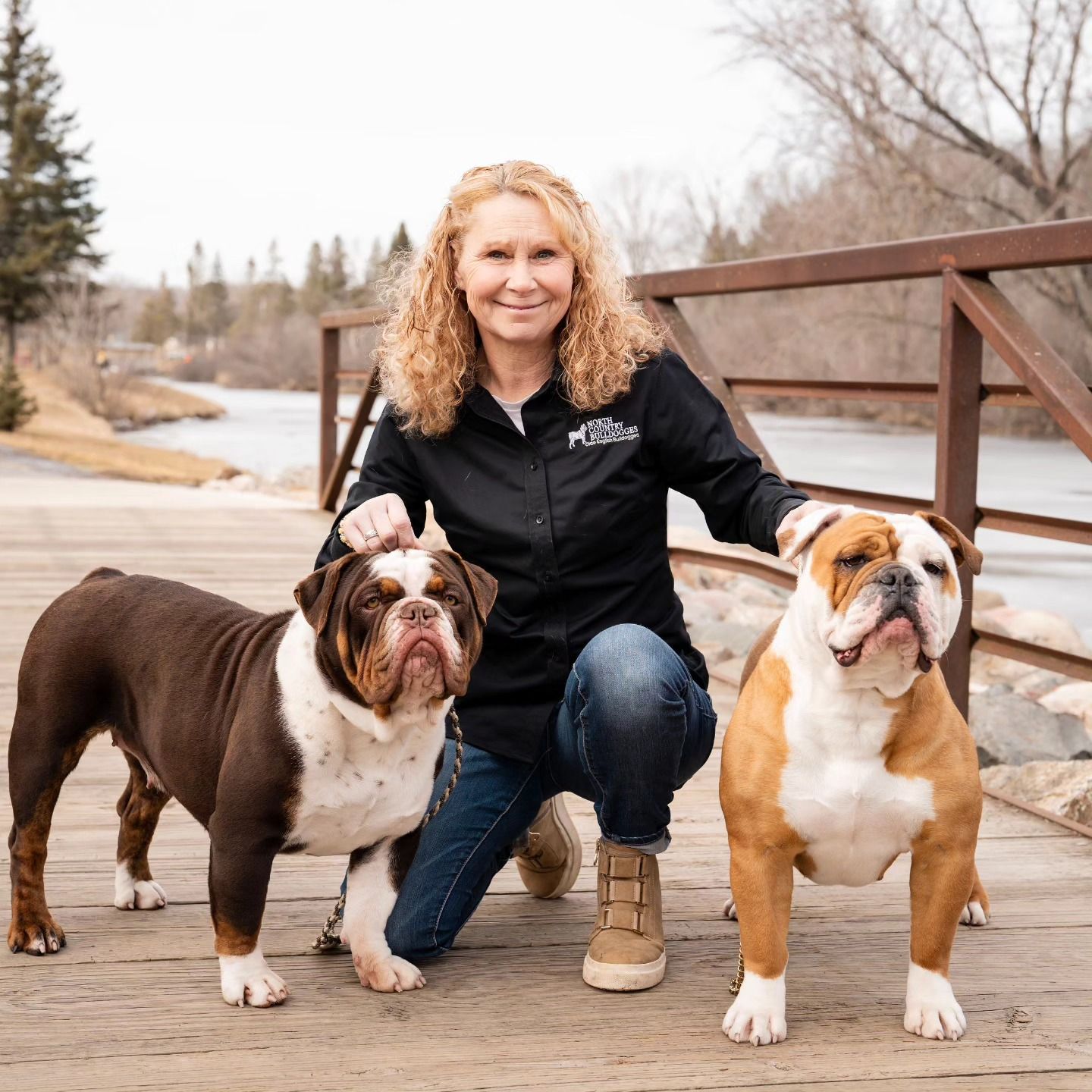 A woman is kneeling down next to two dogs on a bridge