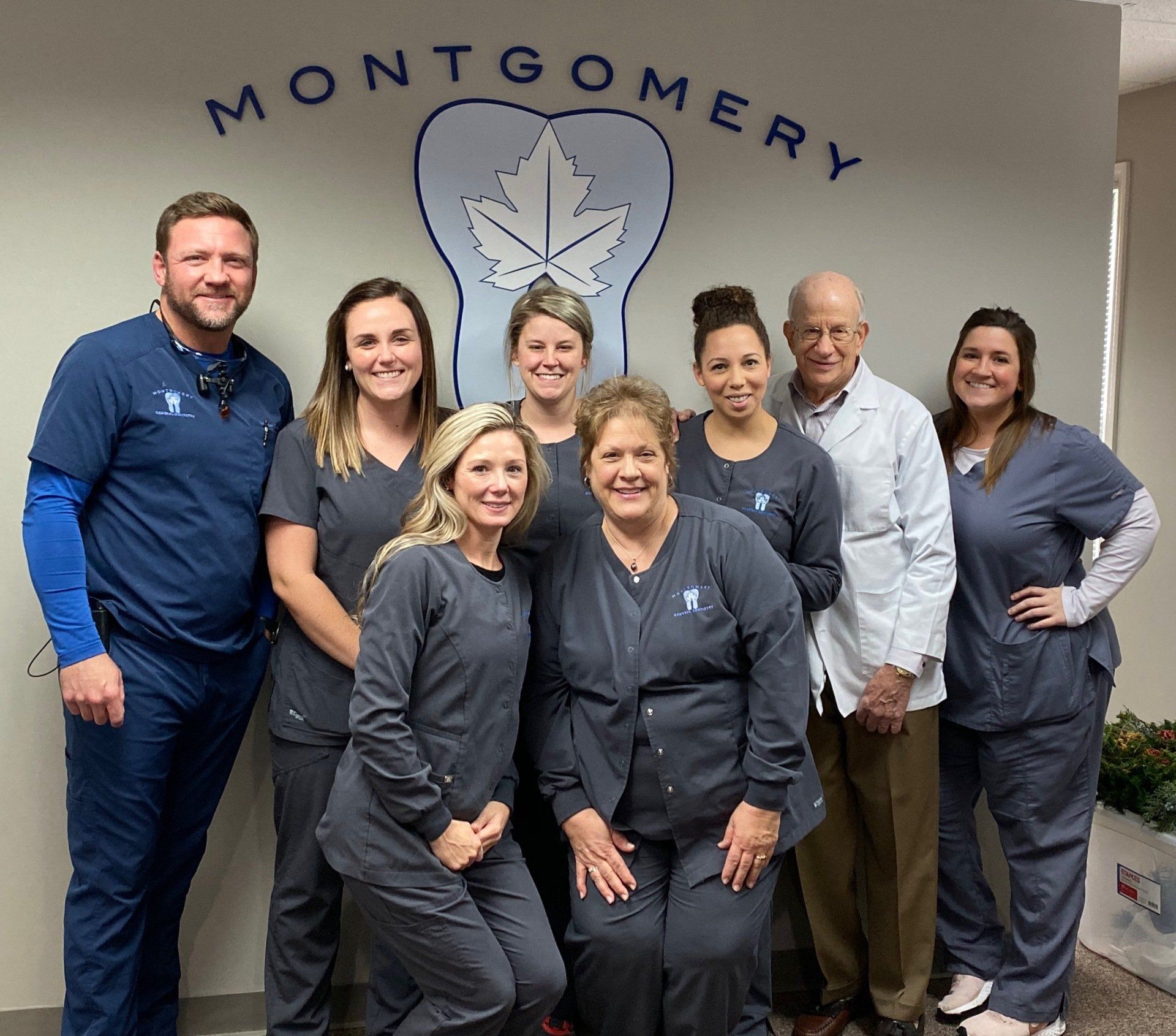 Dr. Heck, of Montgomery General Dentistry in Montgomery, OH and his employees in front of a Montgomery General Dentistry sign inside their office