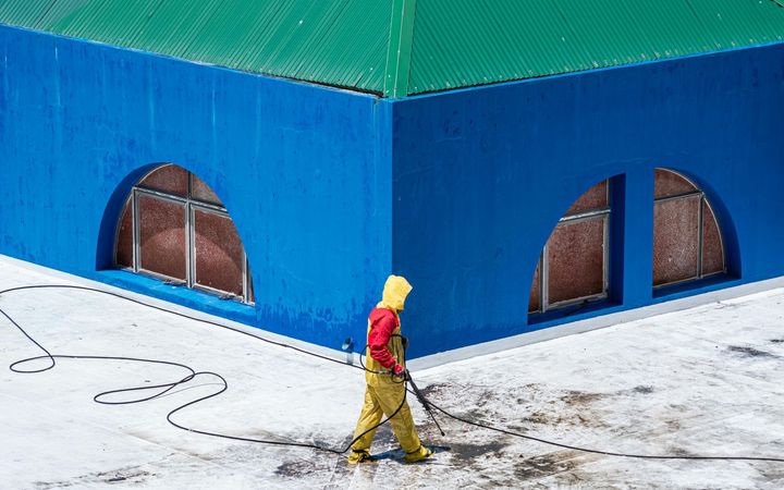 Person in yellow and pink walks past a blue building with arched windows on a snowy street.