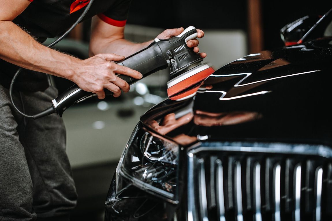 A Man is Polishing a Black Car With a Machine