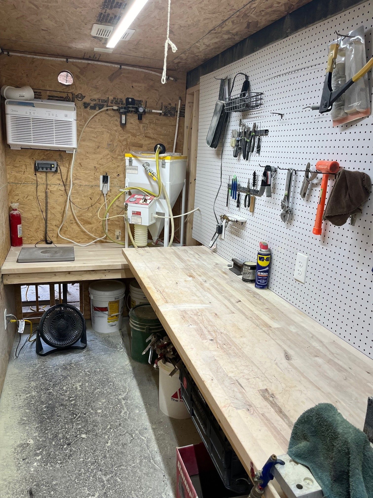 A wooden workbench in a garage with tools hanging on the wall.