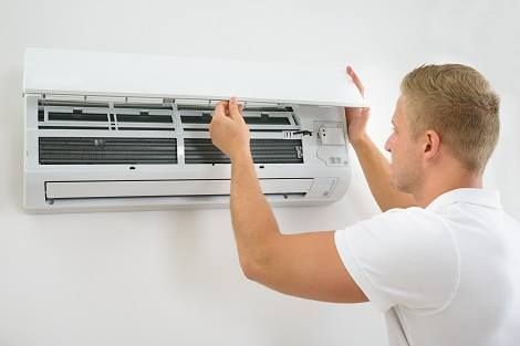A man is installing an air conditioner on a wall.