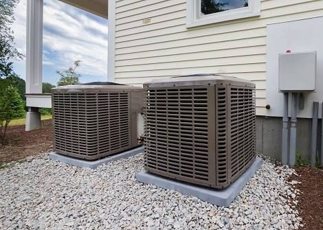 Two air conditioners are sitting on the side of a house.