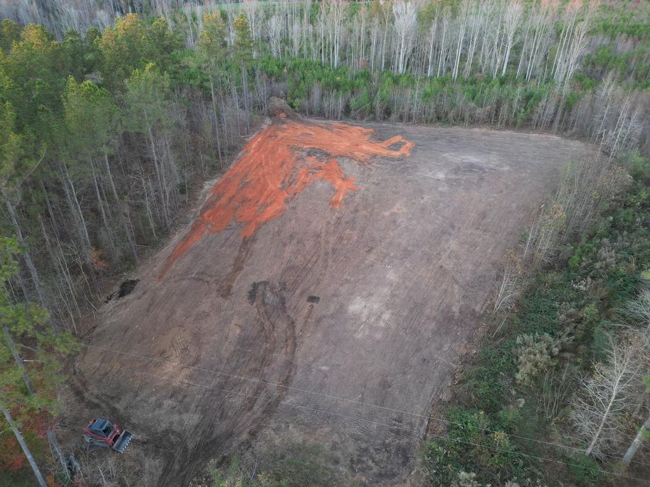 An aerial view of a dirt field in the middle of a forest.