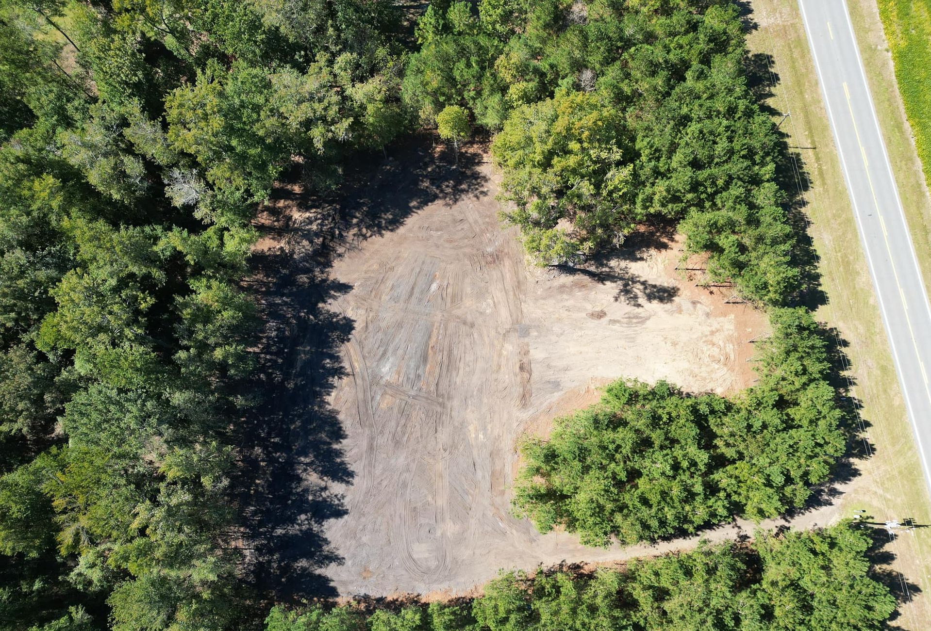 An aerial view of a field surrounded by trees and a road
